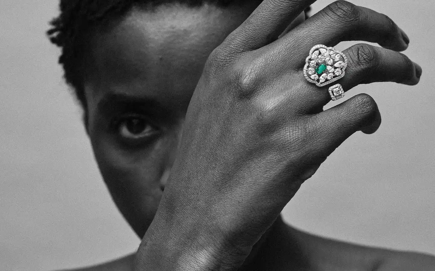Woman wearing 18K recycled white gold ring with marquise, oval, round, pear and princess-cut white diamonds, Zambian emerald.