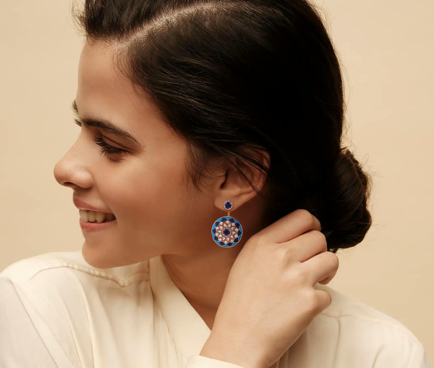 Woman wearing 18K recycled rose-gold earrings with lapis and turquoise inlay, pear and cushion-cut diamonds and iolites.